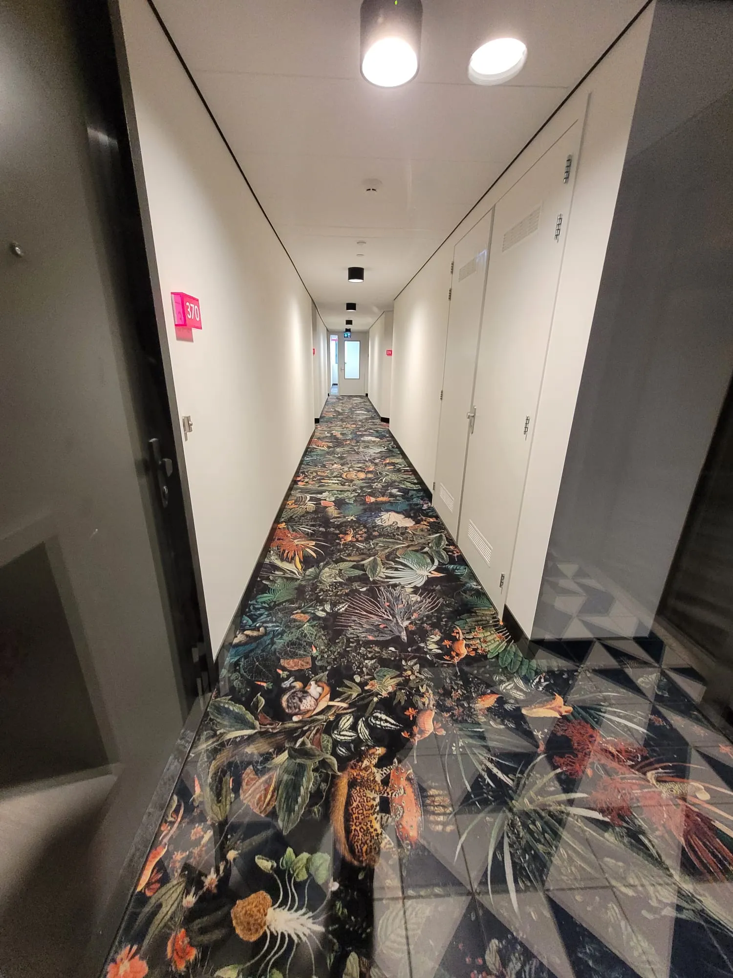 Hotelgang met wandpanelen, zwarte plinten en tapijtvloer